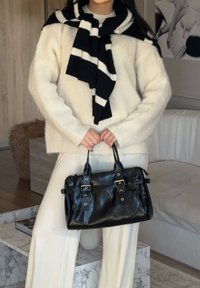 Black leather handbag with two top handles, silver hardware, and buckle accents; teamed with a cream fluffy sweater and striped scarf.