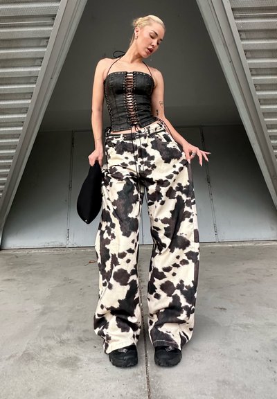 Top de corsé de mezclilla negra con cordones en el frente; pantalones sueltos con estampado de vaca en crema y negro; zapatos negros texturizados; accesorios mínimos.