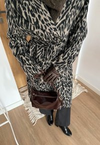 Personne portant un manteau à imprimé léopard noir et blanc, des gants en cuir marron, tenant un sac à main marron, un pantalon noir et des chaussures noires brillantes à l'intérieur.