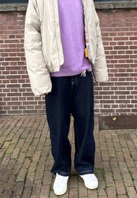 Beige donsjack met garnalenkraag over een lavendelkleurige gebreide trui, gecombineerd met losse donkere denimbroeken en witte sneakers; voorzien van een taille met trekkoord.