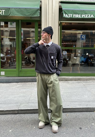 Camisa negra de manga larga con rayas verticales y bolsillo en el pecho, combinada con pantalones de pierna ancha color verde claro y zapatos beige.