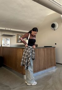 Μαύρο τοπ με καφέ λουλουδάτα μακριά μανίκια, γκρίζα τζην και καρό πουκάμισο δεμένο στη μέση. Λευκά sneakers και μια μικρή λευκή τσάντα.