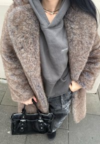 Καφέ ψεύτικο γούνινο παλτό με φαρδύ γιακά, γκρι φούτερ, μαύρη υφασμάτινη τσάντα και τζιν παντελόνι με άσπρες ραφές. Κ casual στιλ με πολλές στρώσεις.