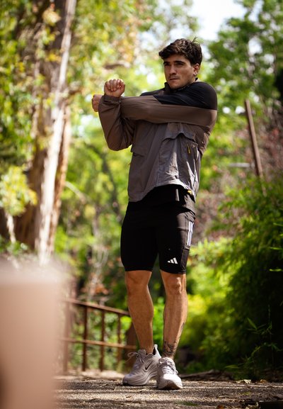 Hombre en ropa deportiva estirando los brazos al aire libre en un camino boscoso durante el día.