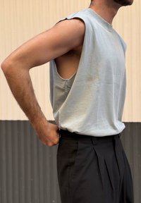 Gaiši zils bez piedurknēm tops ar neapstrādātām rokas atverēm, apvienots ar melnām dūrējošām biksēm. Audums šķiet mīksts un nedaudz teksturēts.