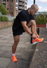 Erksed oranžid jooksujalatsid, millel on võrgust ülaserv ja kontrastsed mustad detailid. Jalatsil on pehmendusega tald ja seda kinnitab sidumine inimene.