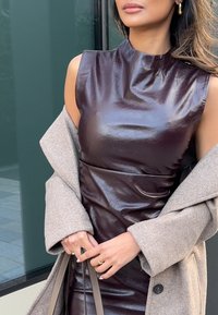 Vestido sem mangas bordeaux brilhante com gola alta, combinado com um casaco cinza claro. Apresenta uma textura suave e costuras laterais curvas.