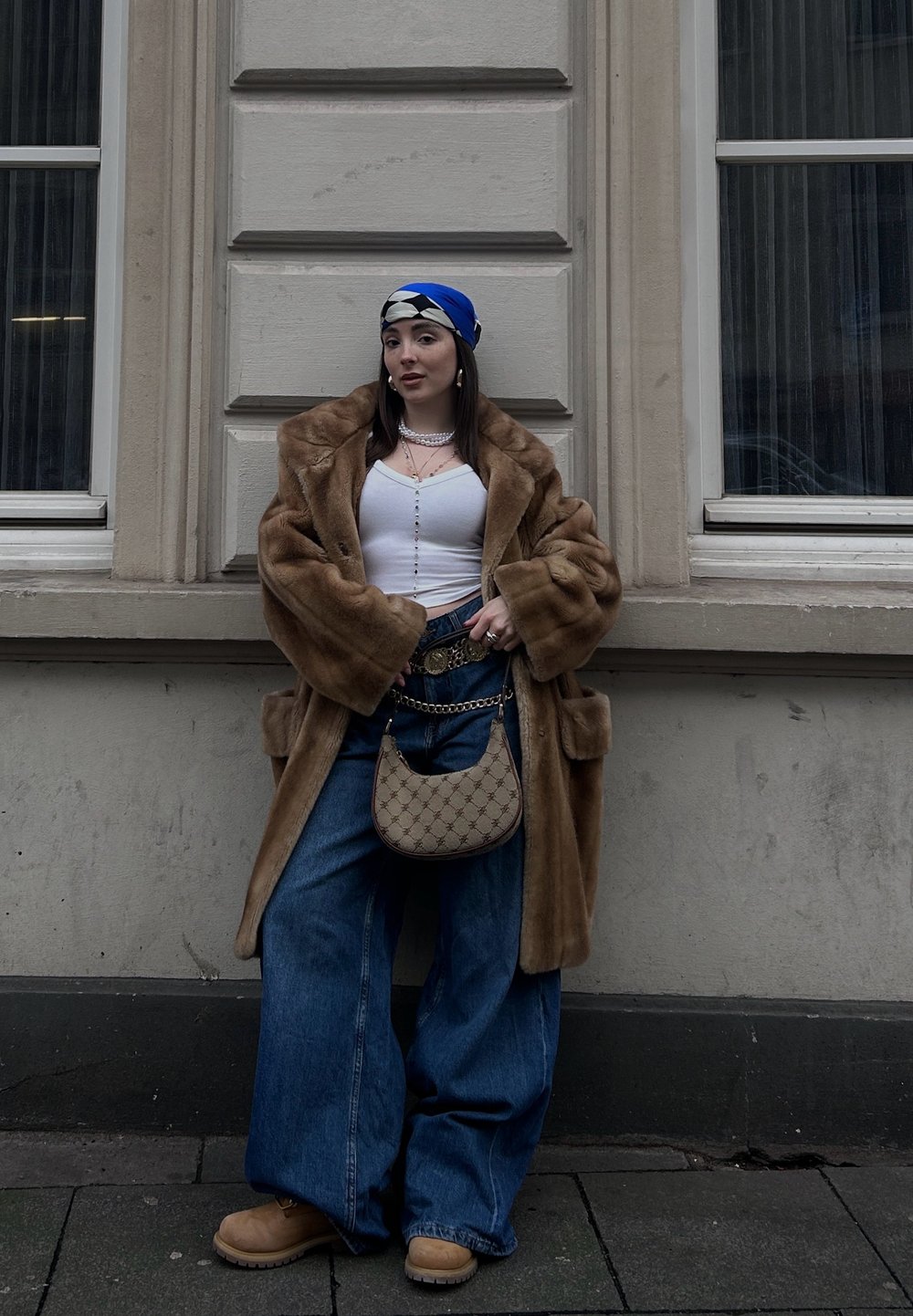 Καφέ ψεύτικο παλτό γούνας, λευκή εφαρμοστή μπλούζα, υπερμεγέθες μπλε τζιν παντελόνι, ταμπά μπότες και μια κασκόλ με σχέδιο σε μπλε και λευκό. Τονίζεται με μια μπεζ τσάντα χεριού.