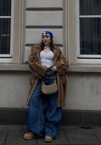 Καφέ ψεύτικο παλτό γούνας, λευκή εφαρμοστή μπλούζα, υπερμεγέθες μπλε τζιν παντελόνι, ταμπά μπότες και μια κασκόλ με σχέδιο σε μπλε και λευκό. Τονίζεται με μια μπεζ τσάντα χεριού.