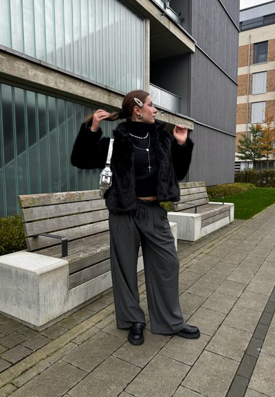 Chaqueta de felpa negra, top de punto negro, pantalones de pierna ancha grises y botas gruesas negras. Accesorios plateados, incluyendo un bolso y joyería.
