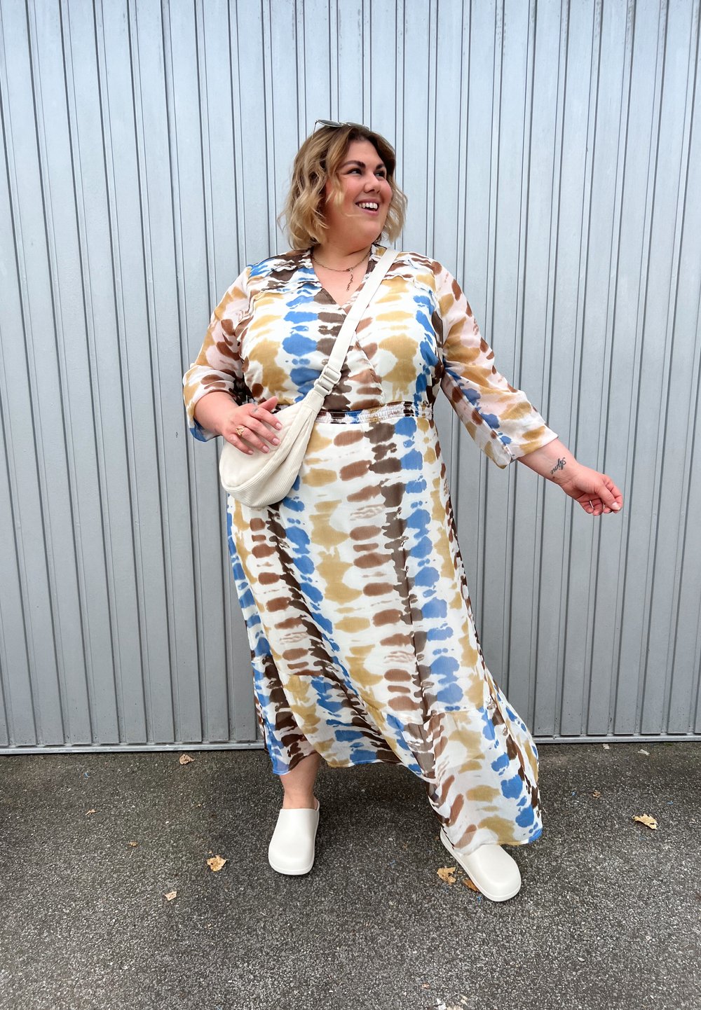 Dlouhé, splývavé šaty v béžové, modré a hnědé tie-dye vzoru. Mají tříčtvrteční rukávy a naškrobený pas. V kombinaci s bílými dřeváky.