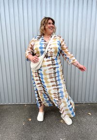 Dlouhé, splývavé šaty v béžové, modré a hnědé tie-dye vzoru. Mají tříčtvrteční rukávy a naškrobený pas. V kombinaci s bílými dřeváky.