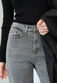 Kõrge vöökohaga hallid teksapüksid, mis on kaunistatud naelutud mustriga. Kaasa on must pikikleit ja jakk.