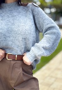 Grå strikket sweater med høj krave, parret med brune bukser og et brunt bælte med en guldbuckle. Fokuser på tekstur og farvekontrast.