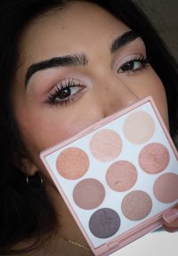 Runde, pastellrosa Make-up-Palette mit neun Farbtönen, darunter schimmernde und matte Finish in warmen Tönen. Die klare Hülle zeigt die Farben deutlich.