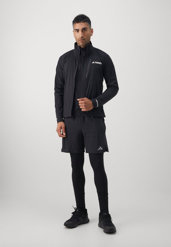Czarny strój sportowy składający się z kurtki na zamek błyskawiczny z teksturowanymi panelami, długimi rękawami, dopasowanej warstwy bazowej, szortów i czarnych sneakersów.