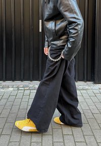 Μαύρο παντελόνι σε φαρδιά γραμμή συνδυασμένο με μαύρη δερμάτινη τζάκετ. Περιλαμβάνει κίτρινες αθλητικές υποδήσεις με άσπρες λεπτομέρειες και ασημένια αλυσίδα.