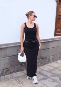 Μαύρο αμάνικο μπλουζάκι και συνδυασμένη μακριά φούστα με σπάγγο, συνδυασμένα με λευκή υφασμάτινη τσάντα και γκρι αθλητικά παπούτσια. Λείος ύφασμα, χαλαρός σχεδιασμός.