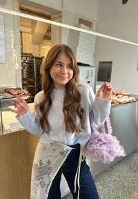 Cardigan grigio in maglia con orlo smerlato, abbinato a jeans scuri. La borsa lilla chiaro con volant e i dettagli in pizzo completano il look.