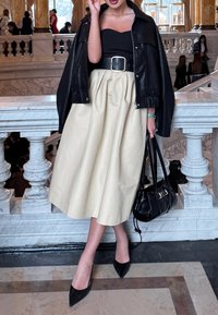 Μαύρο δερμάτινο μπουφάν πάνω από μαύρη μπλούζα, σε συνδυασμό με κρεμ φούστα μέχρι το γόνατο και μαύρες μυτερές γόβες. Περιλαμβάνεται μαύρη τσάντα.