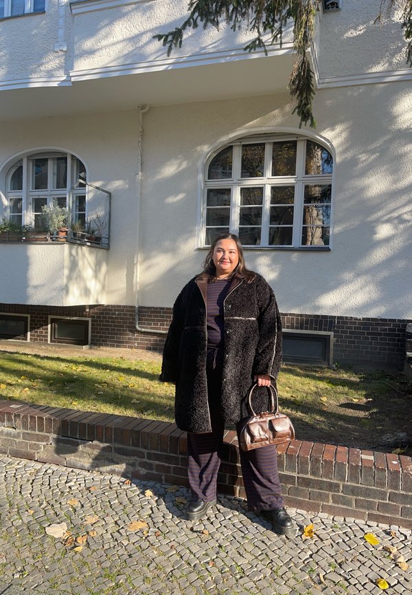 Svart fluffy kåpe med brune detaljer, marineblå stripete topp, matchende bukser og en brun håndveske. Sti av stein i utendørsmiljø.