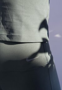 Heledad roheline ribikujuline sporditopp, mis on paaritud sobivate istuvate retuusidega. Retuusidel on väike hall Nike logo vööl.