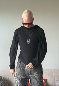 Zwarte, getailleerde langesleeve shirt met een ronde hals en doorzichtig materiaal, gelaagd over een zwarte tanktop met een logo in rhinestones. Camo cargo broek.