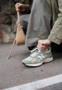 Vaaleanvihreät New Balance -lenkkarit, joissa on verkko- ja mokkanahkatekstuuri, valkoiset yksityiskohdat ja pehmustettu kaulus, nauhoitettuna päällystetylle pinnalle.