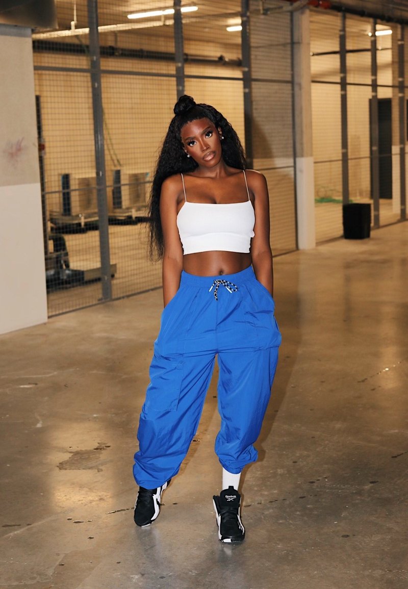 Blue cargo trousers with elasticated cuffs, teamed with a white cropped tank top. The outfit includes a drawstring waistband and trainers.