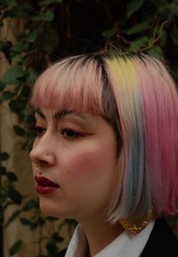 Farverigt pastelhår med nuancer af pink, gul og blå, stylet i en bob med lige pandehår; prydet med en stor guldring og veldefineret makeup.