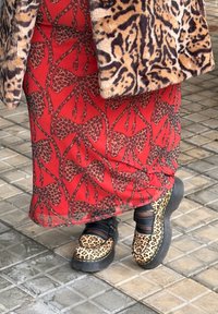 Manteau à imprimé léopard en fourrure, jupe rouge avec grand nœud et motif à taches léopard, ainsi que chaussures compensées à imprimé léopard avec brides noires.