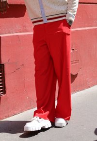 Κόκκινοι παντελόνες με φαρδύ πόδι φτιαγμένες από ελαφρύ ύφασμα, με απαλή υφή και χαλαρή εφαρμογή, συμπληρωμένες με χοντρές λευκές αθλητικές παπούτσια.