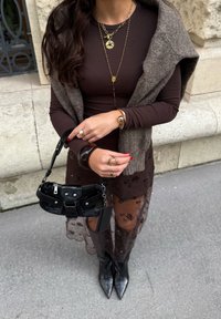Hnedý dlhý rukáv top vrstvený so šedým šálom, kvetinová čipková sukňa, čierne členkové čižmy a malá čierna taška. Zlato-hnedé doplnky.