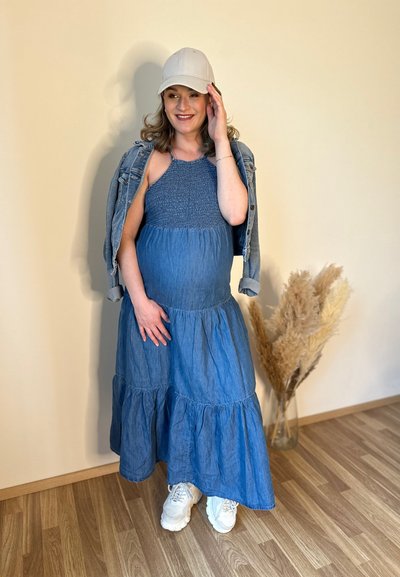 Vestido de denim con un corsé fruncido, volantes en capas y un color azul claro. Combinado con una chaqueta de denim y zapatillas blancas.