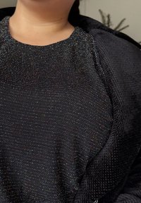 Sort top med en tekstureret overflade med flerfarvede prikker, rund halsudskæring og korte ærmer. Bær under en sort blød jakke.