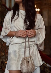 Haut en tissu léger marbré avec des manches fluides, associé à une jupe assortie. Tient un petit sac à main métallique scintillant avec une bandoulière en chaîne.