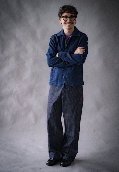 Chaqueta de mezclilla en tono azul oscuro, combinada con pantalones holgados de corte amplio en azul marino, que presentan un diseño sutil de puntos y un acento rojo.