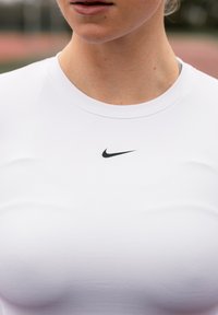 Vit sporttröja i stretchtyg med en svart Nike-logotyp ovanför halslinningen, figursydd modell och slät textur.