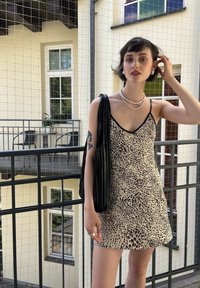 Robe mini à bretelles spaghetti en beige avec un imprimé abstrait sombre. Elle présente un décolleté en V peu profond et une coupe décontractée, associée à un sac plissé noir.