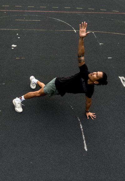 Hombre realizando una plancha lateral sobre una superficie de goma negra, vistiendo una camiseta negra, pantalones cortos verdes y zapatillas deportivas blancas con detalles rojos.