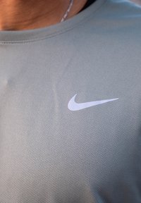 Lys grå kortermet trenings-T-skjorte med teksturert stoff. Har en hvit Nike-logo på brystet.