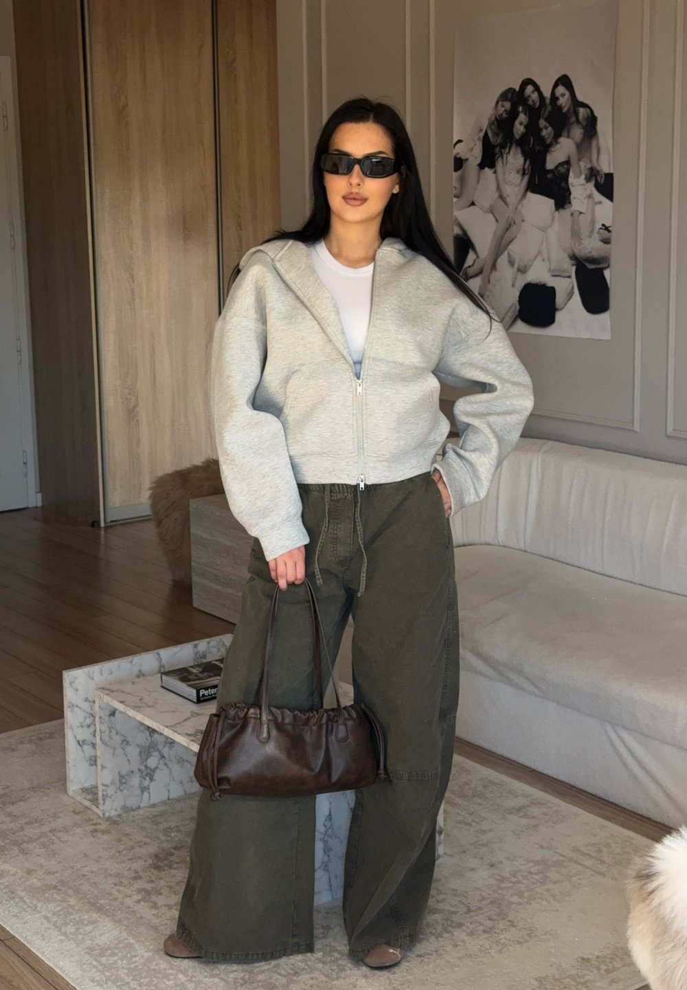 Grigia felpa con zip, t-shirt bianca, pantaloni oversized verde oliva, borsa marrone con dettagli arricciati e occhiali da sole neri.