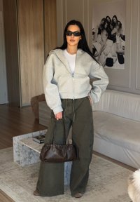 Grigia felpa con zip, t-shirt bianca, pantaloni oversized verde oliva, borsa marrone con dettagli arricciati e occhiali da sole neri.