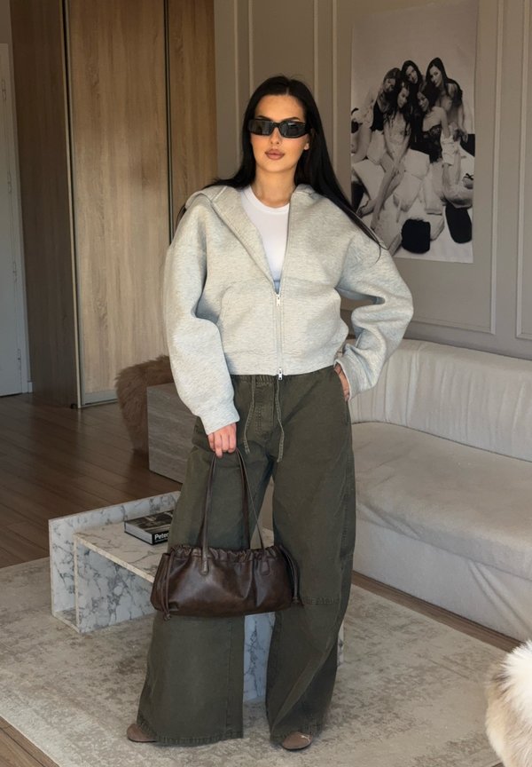 Grigia felpa con zip, t-shirt bianca, pantaloni oversized verde oliva, borsa marrone con dettagli arricciati e occhiali da sole neri.