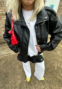 Svart skinnbikerjakke, hvit t-skjorte, svarte og hvite sportslige shorts og gule slip-on-sko. Rød veske med kjedestropp og nøkkeltilbehør.