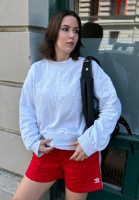 Γκρι φούτερ με χαμηλωμένους ώμους, συνδυασμένο με κόκκινες αθλητικές βερμούδες με λευκές ρίγες. Μαύρη τσάντα με ανθεκτική λωρίδα.