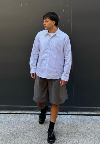 Camisa de botones de manga larga a rayas en azul claro y blanco combinada con pantalones cortos grises hasta la rodilla y zapatos negros con cordones.