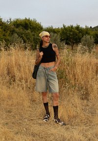 Top scurt negru, pantaloni scurți din denim albastru deschis, ciorapi din plasă negri, pantofi cu imprimeu de vacă, batic galben, colier din lanț auriu, diverse tatuaje.
