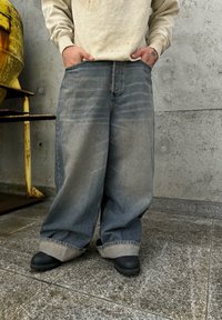 Light grey wide-leg jeans with a faded finish, featuring a rolled hem and pockets, paired with black slip-on shoes.