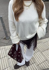 Bijeli pleteni džemper s rebrastim manšetama, nošen preko bordo topa ukrašenog čipkom. Uparen s bordo torbom sa srebrnim zakovicama i svijetlijim hlačama.